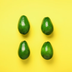 Green avocado pattern on yellow background. Top view. Square crop. Pop art design, creative summer food concept. Organic avocadoes in minimal flat lay style.