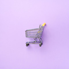 Shopping cart on purple background. Minimalism style. Square crop. Creative design. Top view with...