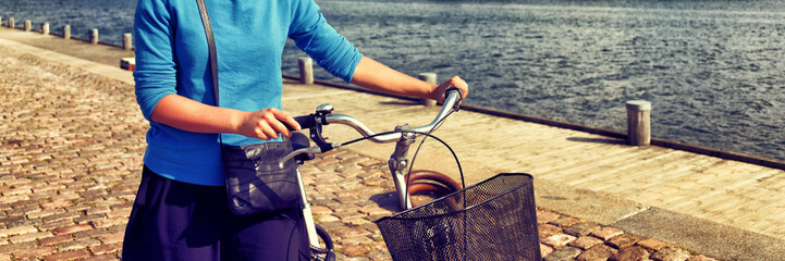 Bicycle commute in city street. Girl biking with bicycle walking on sidewalk in urban harbour old...