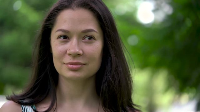 A portrait of a cute asian woman looks thoughtfully. A weak wind blows her hair. Light smile.