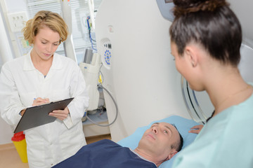 Fototapeta premium Doctor filling in form, patient layed on bed