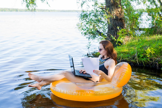 Business woman working on a laptop in an inflatable ring on the river, the concept of working on vacation.