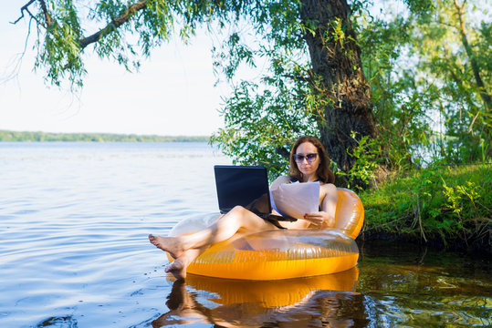 Business woman working on a laptop in an inflatable ring on the river, the concept of working on vacation.