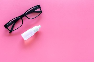 Eye drops in small bottle near glasses on pink background top view copy space