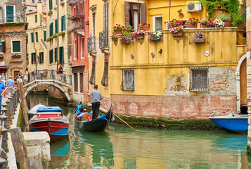 Fototapeta na wymiar Venetian gondolier punting gondola through canal in Venice, Italy