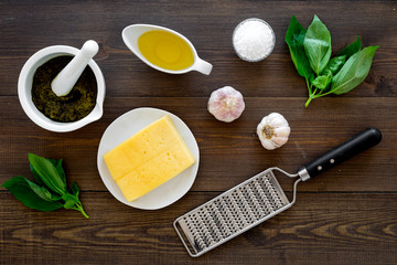 Ingredients for pesto sauce. Cheese, garlic, green basil, olive oil, salt near grater and mortar on...