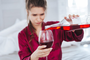 Pouring wine. Emotional nervous woman feeling cheerless while pouring red wine into her glass