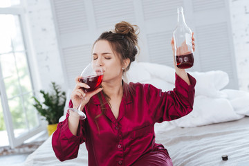 After workday. Businesswoman tasting wine after busy workday while sitting on her bed wearing pajama