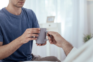 Warm tea. Close up of strong male hands carrying cup and posing on blurred background