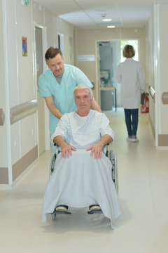 nurse taking senior man patient in wheelchair at hospital corridor