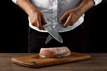 Hands of the chef closeup sharpens a kitchen knife on a knife against a dark background. The concept of cooking, cooking, recipe dishes.