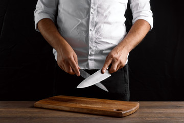 Hands of the chef closeup sharpens a kitchen knife on a knife against a dark background. The concept of cooking, cooking, recipe dishes.