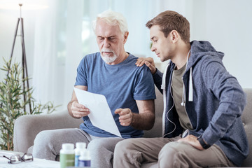 Fototapeta premium Explain this. Serious senior man showing paper to man and sitting on couch