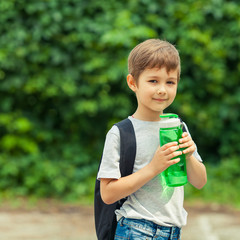 Little boy drinking water from a bottle, hot summer. Child is traveling with a backpack. Vacation in the woods.