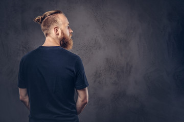 Obraz na płótnie Canvas Back view of a redhead bearded man dressed in a black t-shirt. Isolated on the dark textured background.