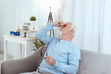 Low blood pressure. Tired senior man touching nose bridge and holding glasses