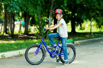 Obraz na płótnie Canvas Little boy learns to ride a bike in the park near the home. Portrait of a cute kid on bicycle. Happy smiling child in helmet riding a cycling.