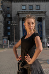 Young blonde woman in sport outfit iluminated by golden sunrays looking into the distance with urban landscape in the background