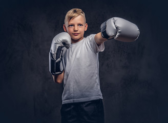 Schoolboy boxer with blonde hair dressed in a white t-shirt wearing boxing gloves shows a boxing...