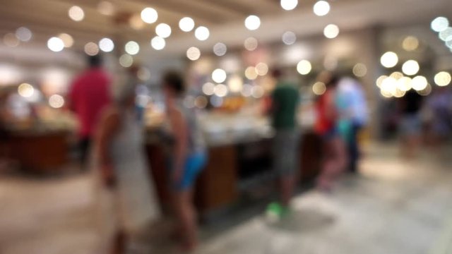 Visitors in the restaurant are out of focus. Defocused image of people, bokeh, lights inside the buffet restaurant.