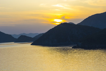 Mediterranean landscape. Sunset on the sea with flowing bright colored rays of the sun through the clouds. Silhouettes of mountains.  Background.