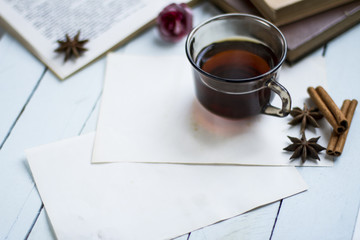 Cup of hot tea, photographed at 45 degrees on the blue wooden table with star anise and cinnamon sticks, red flowers on the decor and stacked books