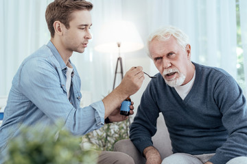 Spoon with medication. Tender man holding spoon while senior man opening mouth
