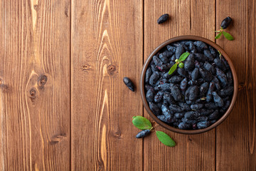 Honeysuckle berries or Lonicera caerulea in ceramic bowl on wooden background © nesavinov
