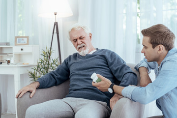 Obraz premium Health state. Tired senior man sitting in armchair and looking at medication