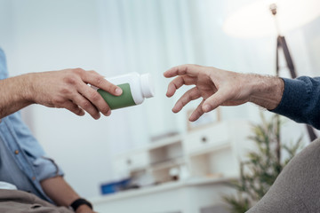 Fototapeta premium Saving medication. Close up of tensed male hand stretching for bottle filled with pills