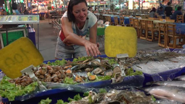 The woman takes shells with shellfish from the counter with seafood. Street food