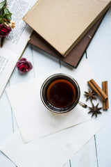 Cup of hot tea photographed from top to bottom on blue wooden table with star anise and cinnamon sticks, red flowers on decoration and stacked books