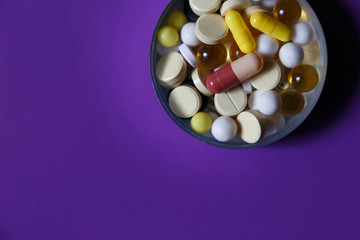 Assorted pharmaceutical medicine pills, tablets and capsules on purple background. Copy space for text