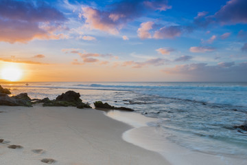 Sunset over Sunset Beach on the North Shore of Oahu, Hawaii with surf rolling in over coral rocks on the sandy beach