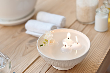 Fototapeta na wymiar spa set with candles in aroma bath and rolled towels on wooden table.