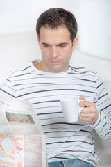 handsome man is reading the newspaper holding a cup
