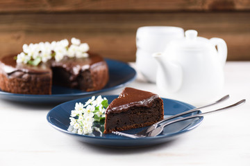 Healthy homemade Siberian dessert. Bird cherry cake with chocolate ganache served with white flowers on white table