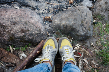 Legs of the girl in yellow sneakers with laces. Stones in the nature