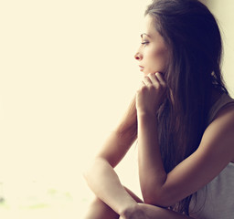 Obraz premium Beautiful sad lonely woman thinking about and looking though the window. Closeup toned portrait