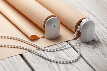 The rolled beige shutters is on a wooden surface. Beige blinds lie on an old wooden white table.