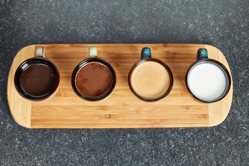 Four coffee cups in a row on a wooden bar displaying different mixtures of milk and coffee