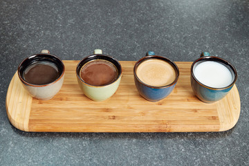 Four coffee cups in a row on a wooden bar displaying different mixtures of milk and coffee