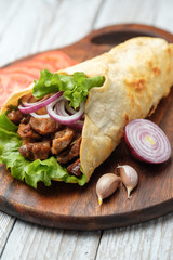 Doner kebab is lying on the cutting board. Shawarma with meat, onions, salad lies on a dark old wooden table.