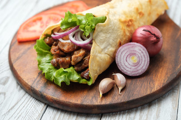 Doner kebab is lying on the cutting board. Shawarma with meat, onions, salad lies on a dark old wooden table.