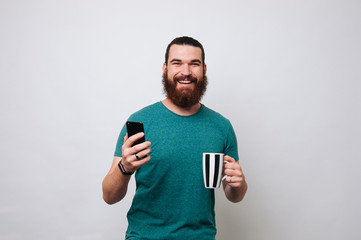 Portrait of happy bearded man holding a phone and drinking tea