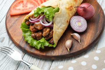 Doner kebab is lying on the cutting board. Shawarma with meat, onions, salad lies on a dark old wooden table.