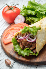 Fototapeta na wymiar Doner kebab is lying on the cutting board. Shawarma with meat, onions, salad lies on a white old wooden table.