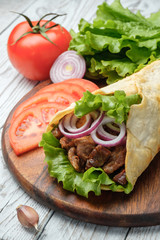 Doner kebab is lying on the cutting board. Shawarma with meat, onions, salad lies on a white old wooden table.