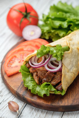 Doner kebab is lying on the cutting board. Shawarma with meat, onions, salad lies on a white old wooden table.