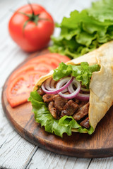 Doner kebab is lying on the cutting board. Shawarma with meat, onions, salad lies on a white old wooden table.